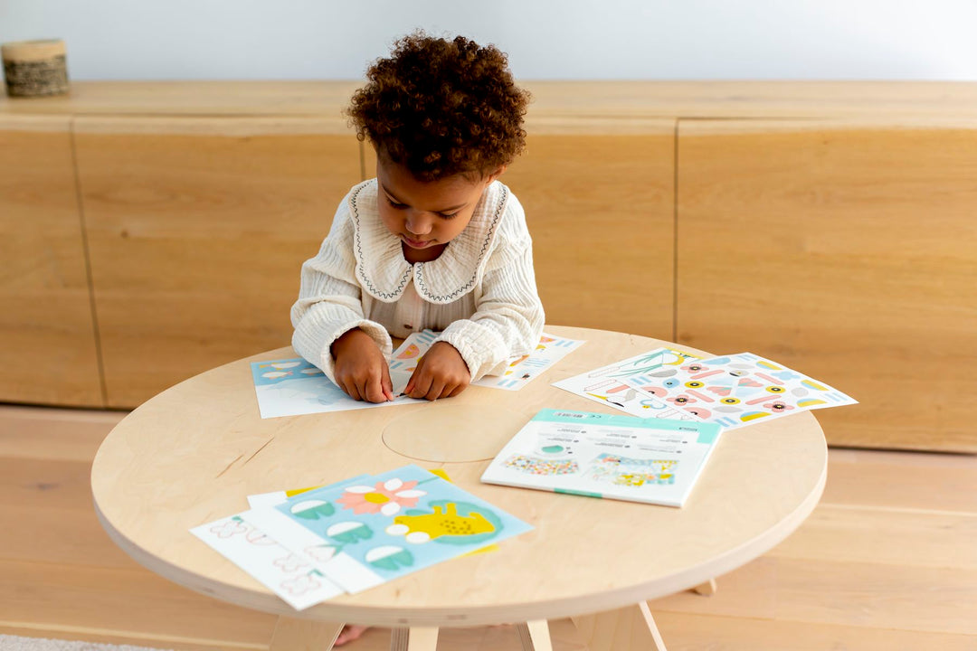Table de dessin Drawin Kid's, dans un salon à la décoration au style scandinave, enfant qui joue sur la table avec des feuilles d'autocollants, Rose et Balthazar
