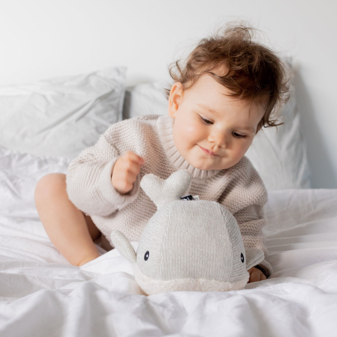 Photo d'un bébé sur un lit qui joue avec la peluche Moby baleine bruits blancs - gris de chez Flow Amsterdam