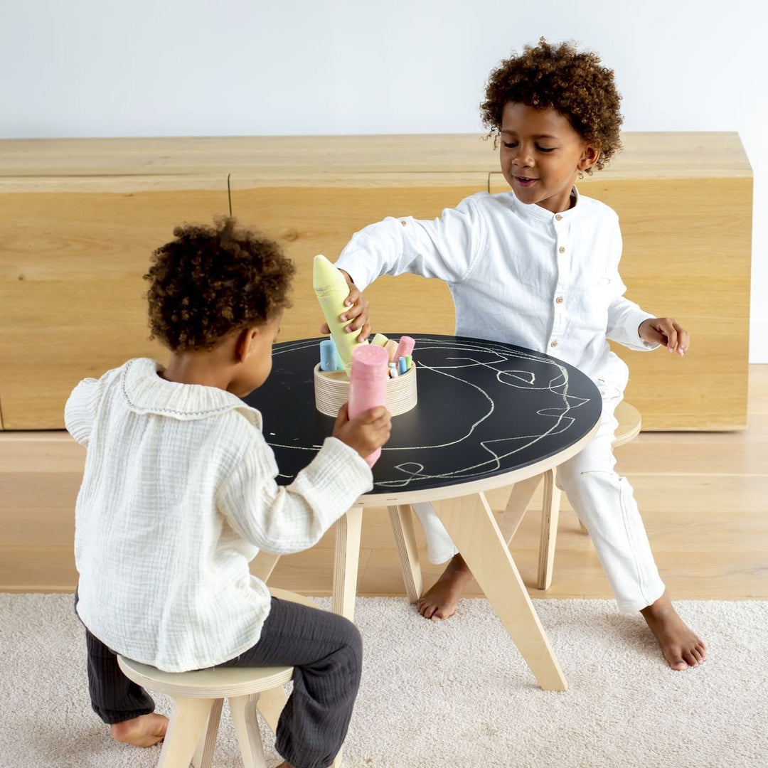 Table de dessin Drawin Kid's, 2 tabourets, dans un salon à la décoration au style scandinave, feuilles de tableau noir à craie, deux enfants dessinent dessus, Rose et Balthazar