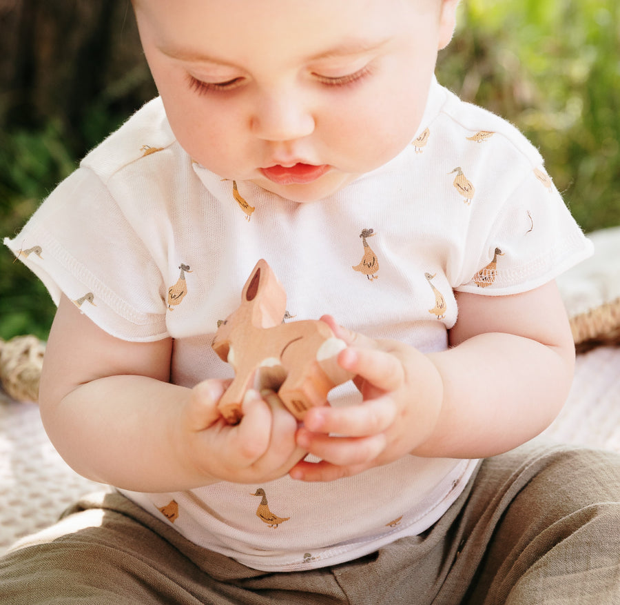 Photo du tee-shirt imprimé canard Mae de chez Les Petites Choses porté par un bébé assis qui à un jouet dans les mains